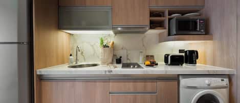Una cocina moderna con armarios de madera, un refrigerador de acero inoxidable, un microondas, un lavamanos y una lavadora integrada.