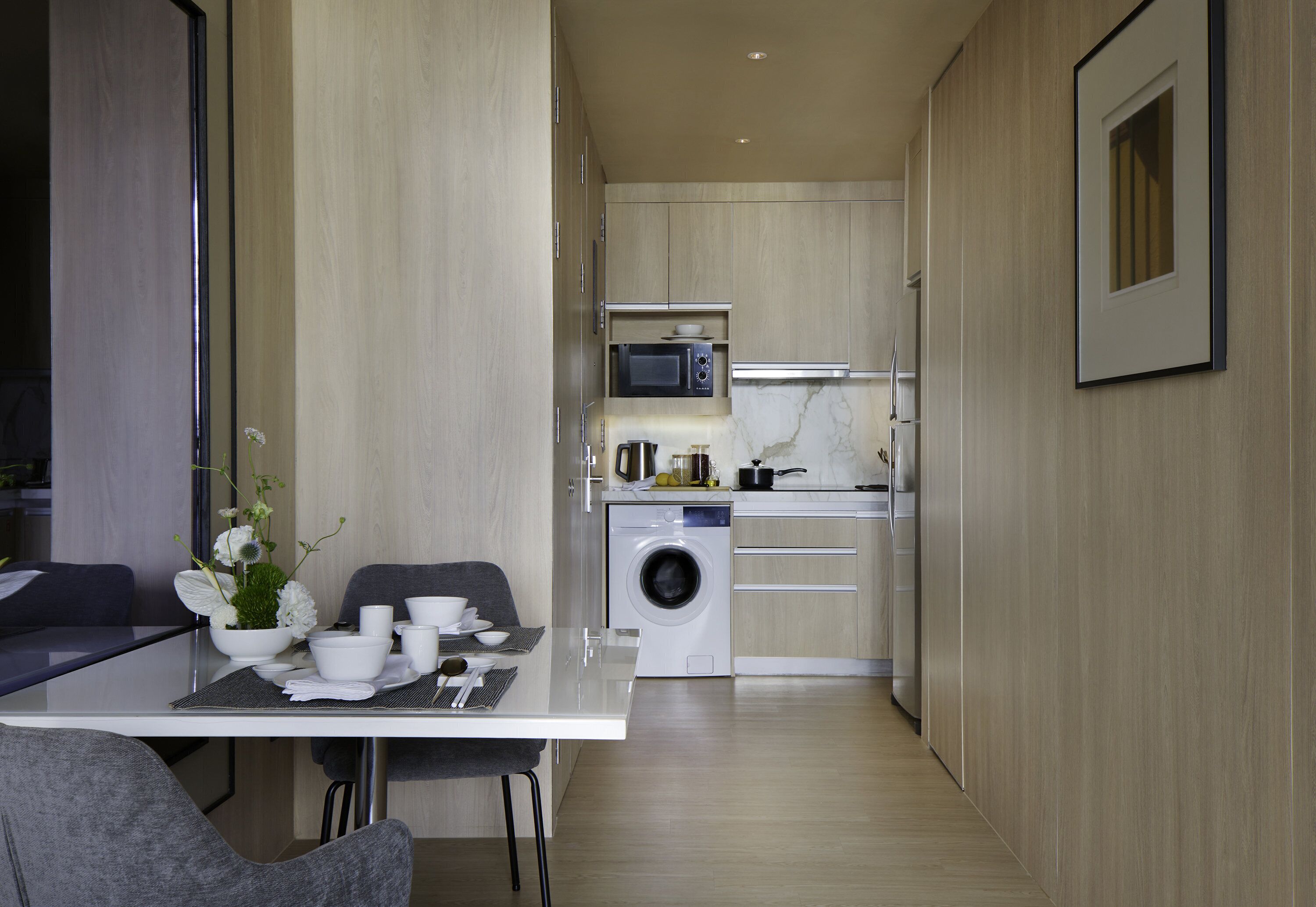 A compact kitchen with a microwave, sink, and washing machine. There is a dining area with a table and chairs.
