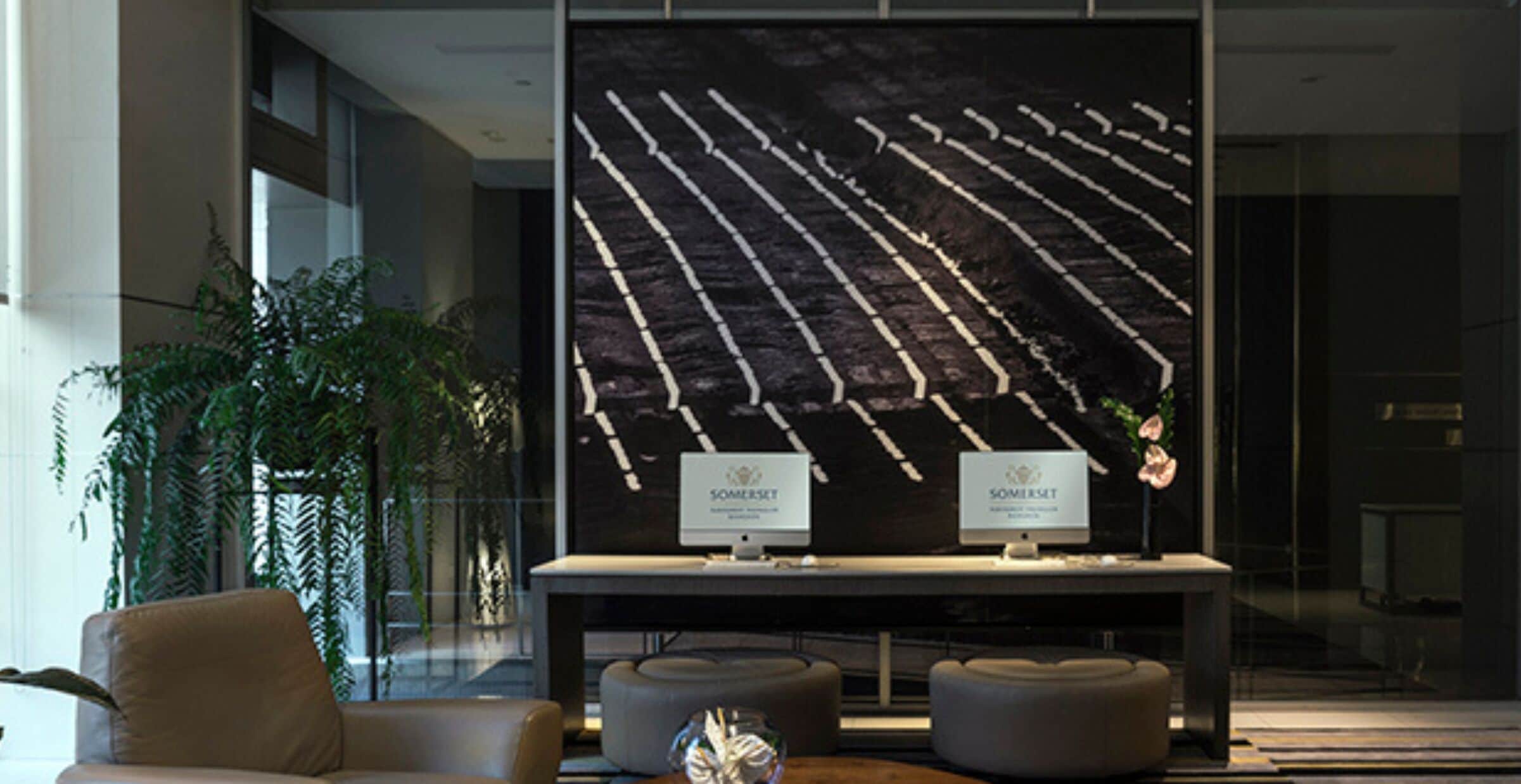 A reception area with a large wall-mounted display, two computer monitors, and a seating area with ottomans.