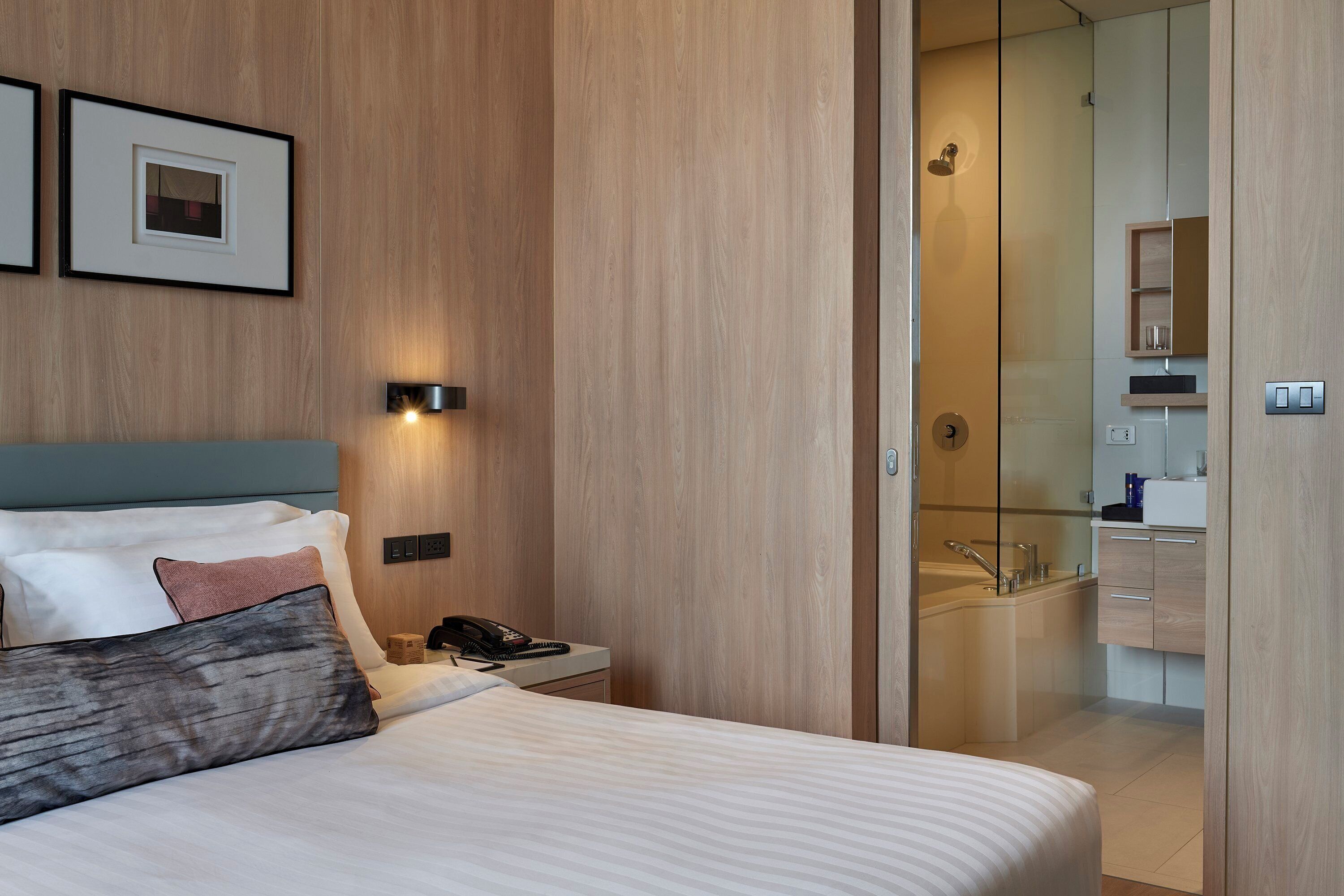A modern hotel room with a large bed, bedside table, and a bathroom visible through an open door.
