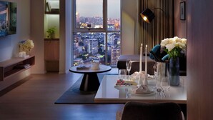 A modern hotel room with a city view, a dining table set with candles, and a cozy seating area. - Somerset Sukhumvit Thonglor Bangkok (Bangkok)