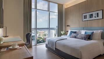 Una habitación de hotel moderna con una cama grande, un escritorio con una computadora portátil, una silla y vistas de la ciudad a través de amplios ventanales.