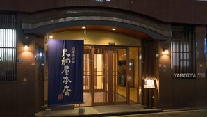 L’entrée d’un hôtel, avec une enseigne indiquant « YAMATOYA, auberge japonaise », et une grande banderole bleue avec du texte blanc.