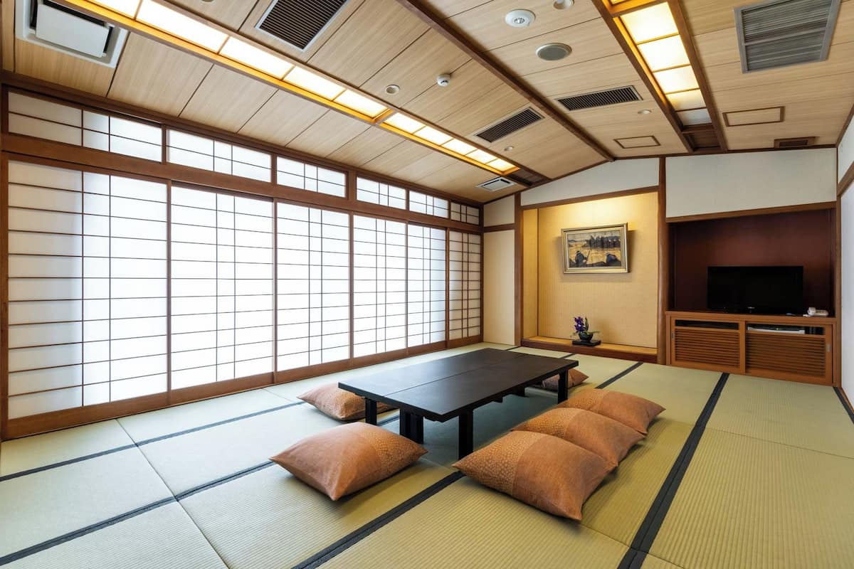 Una habitación japonesa tradicional con suelo de tatami, una mesa baja, cojines, un televisor y un cuadro en la pared.