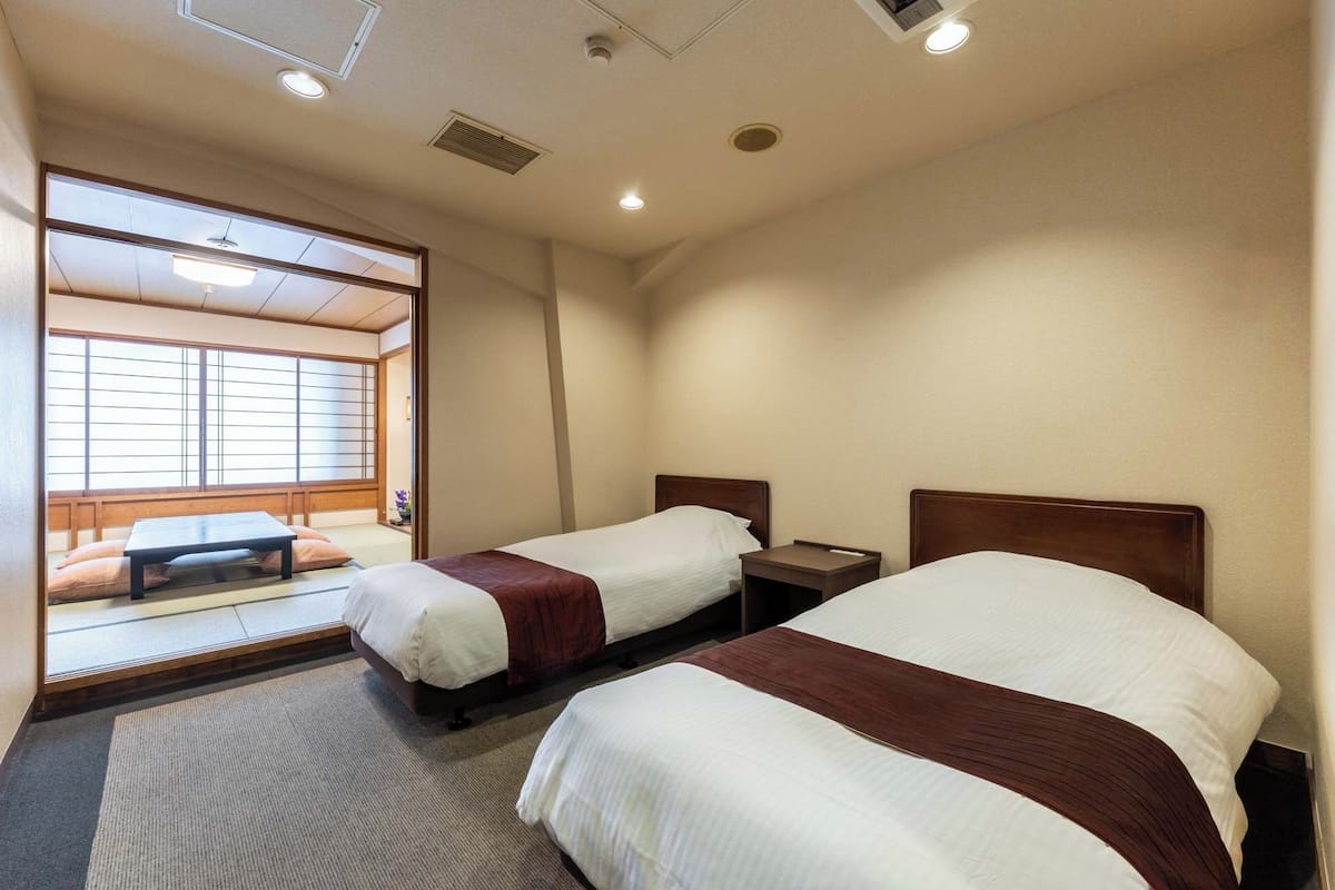 Habitación de hotel con dos camas, una zona de estar con una mesita baja y vistas a través de un celosía japonesa.