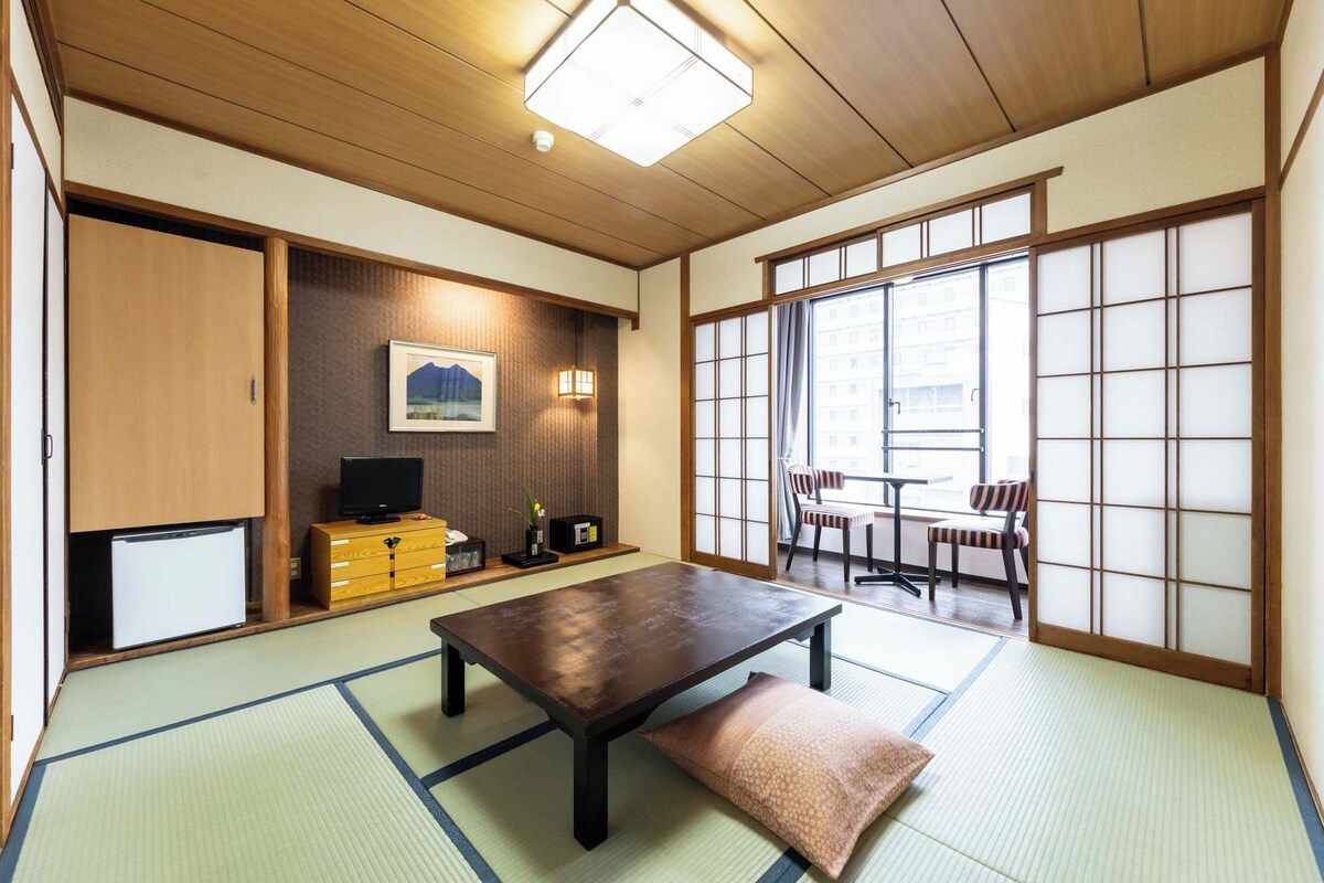 Une pièce de style japonais traditionnel, avec un sol recouvert de tatamis, une table basse, un téléviseur et des portes coulissantes.