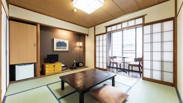 A traditional Japanese room with tatami flooring, a low table, a television, and sliding doors.