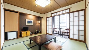 Une pièce de style japonais traditionnel, avec un sol recouvert de tatamis, une table basse, un téléviseur et des portes coulissantes.