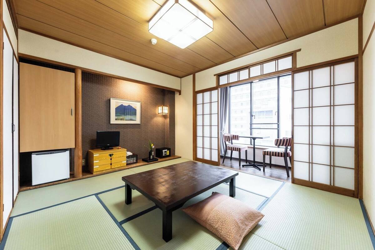 Una habitación japonesa tradicional con suelo de tatami, una mesa baja, un televisor y puertas correderas.