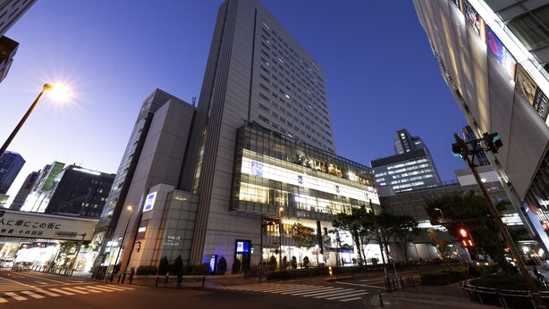 A modern building with a prominent glass facade, multiple floors, and a crosswalk in front. - remm Akihabara (Tokyo)