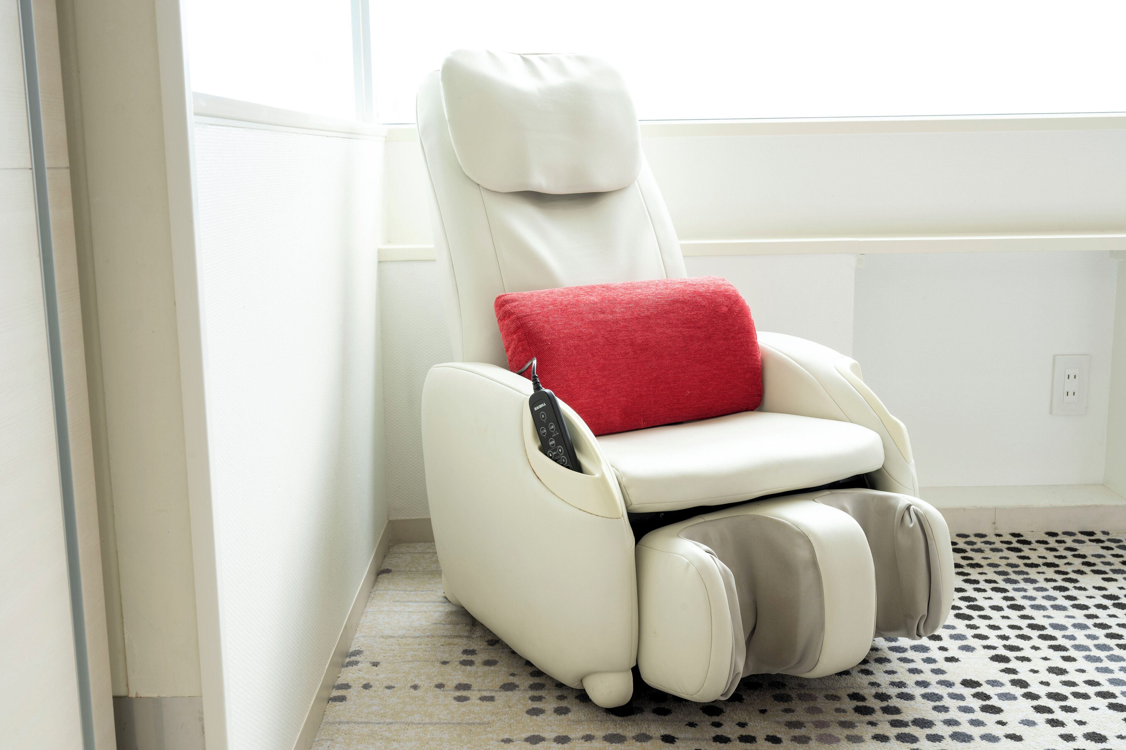 Un fauteuil de massage avec télécommande, un coussin rouge et un tapis à motifs.
