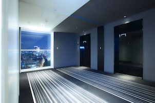 A modern hotel lobby with a large window offering a city view, a striped carpet, and a minimalist design.