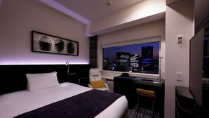 A hotel room with a large bed, a desk, a chair, and a view of the city at night. - remm Akihabara (Tokyo)