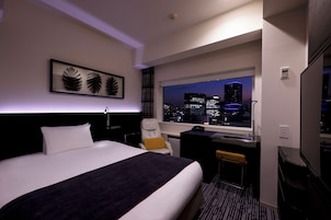 A hotel room with a large bed, a desk, a chair, and a view of the city at night.