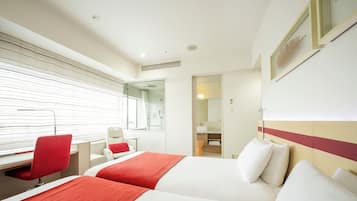 Habitación de hotel con dos camas, un escritorio, una silla y un baño visible a través de una puerta abierta.