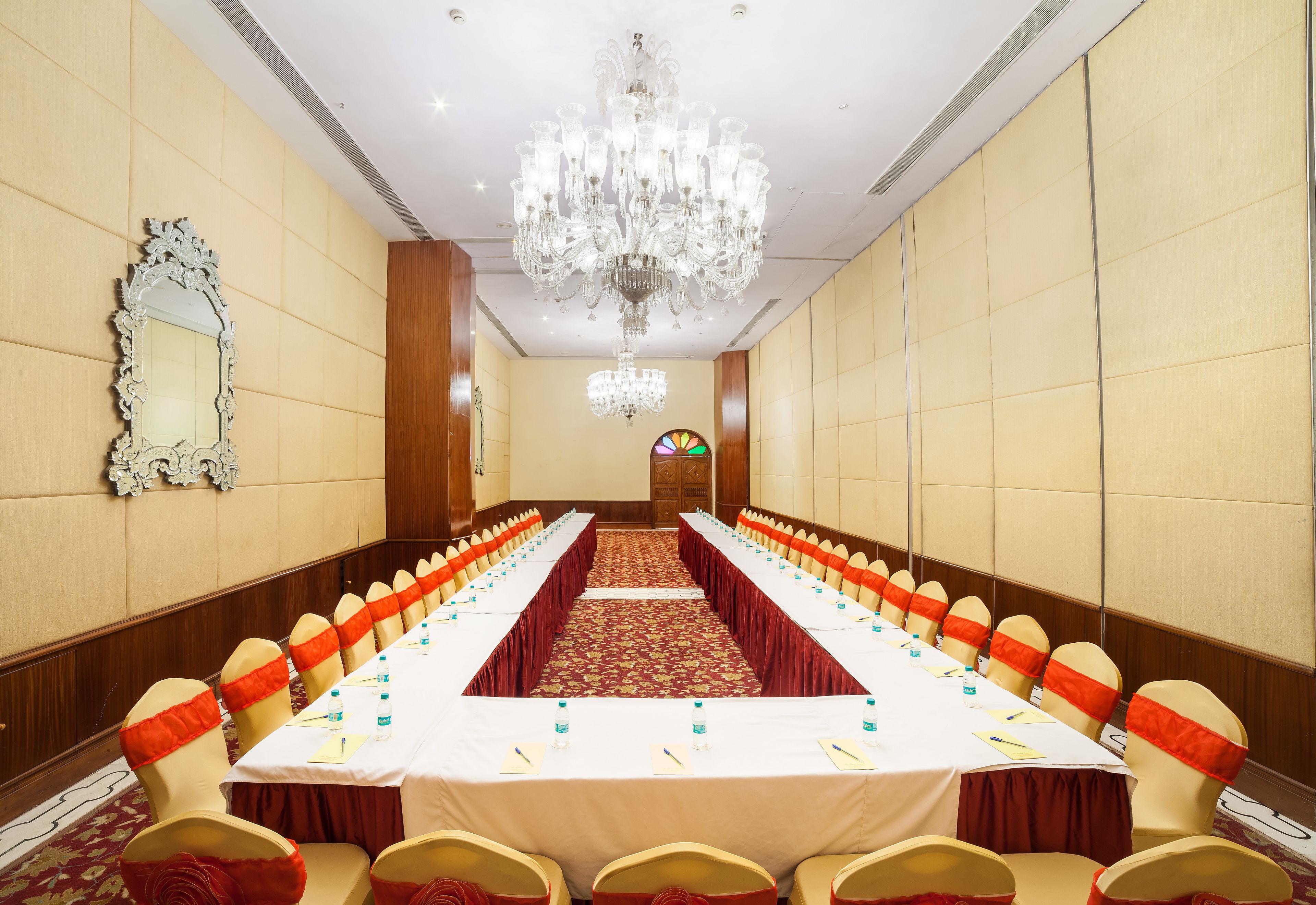 A conference room with a long table, chairs with orange sashes, a chandelier, and a mirror on the wall.