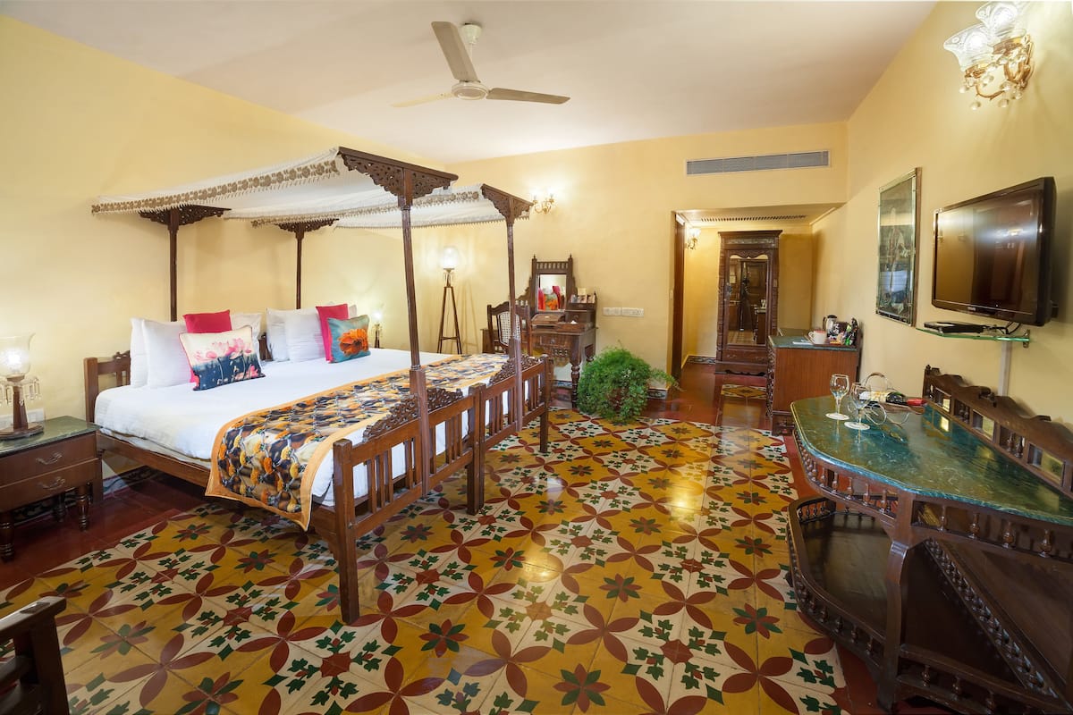 A room with a four-poster bed, a dining table, a television, and a mirror.