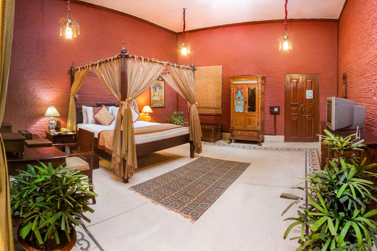 A room with a four-poster bed, a wooden wardrobe, a television, and potted plants.