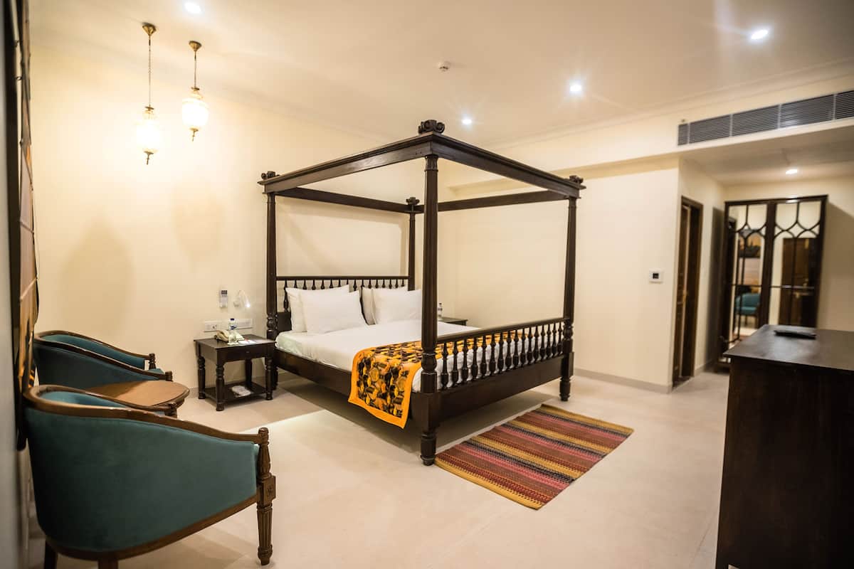 A four-poster bed with a wooden frame, a bedside table, a chair, and a colorful rug.