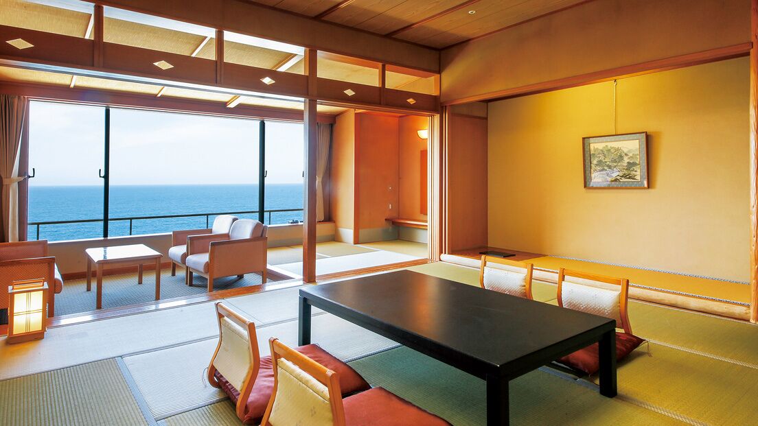 Une pièce avec des tatamis, une table basse, des chaises, une vue sur la mer et un tableau accroché au mur.