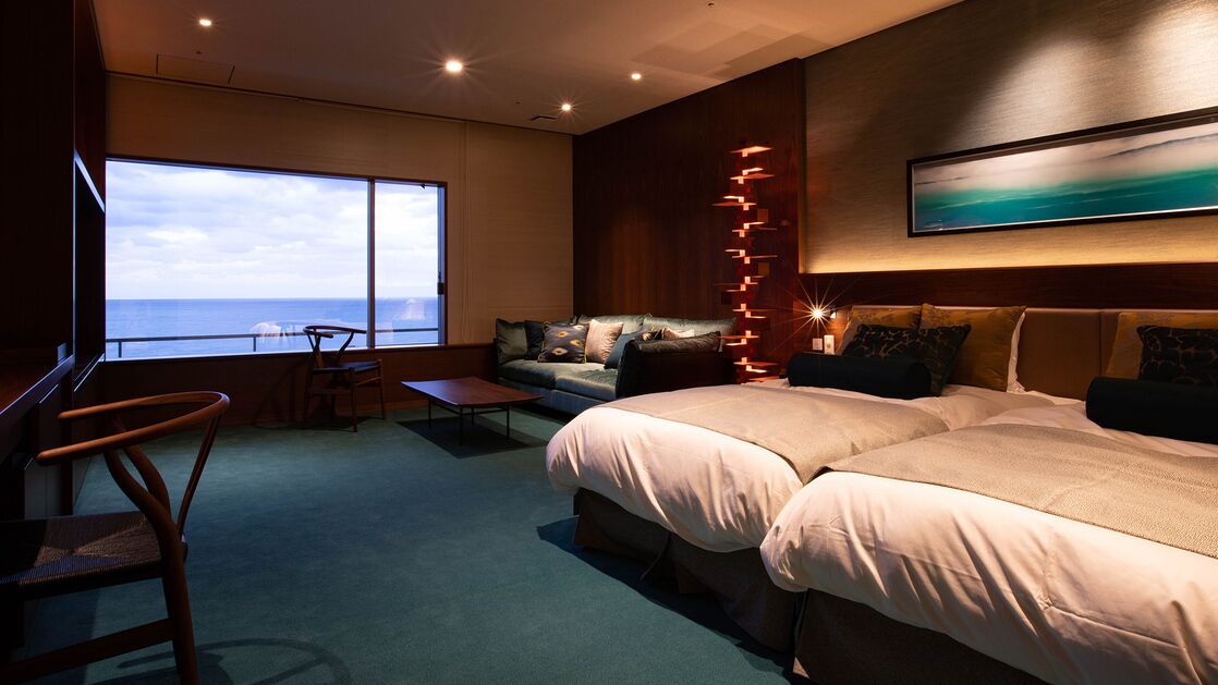 Une chambre d’hôtel moderne, dotée d’un grand lit, d’un canapé, d’un bureau et offrant une vue sur l’océan.