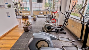 A gym with exercise equipment, a wooden floor, and a view of buildings through large windows.