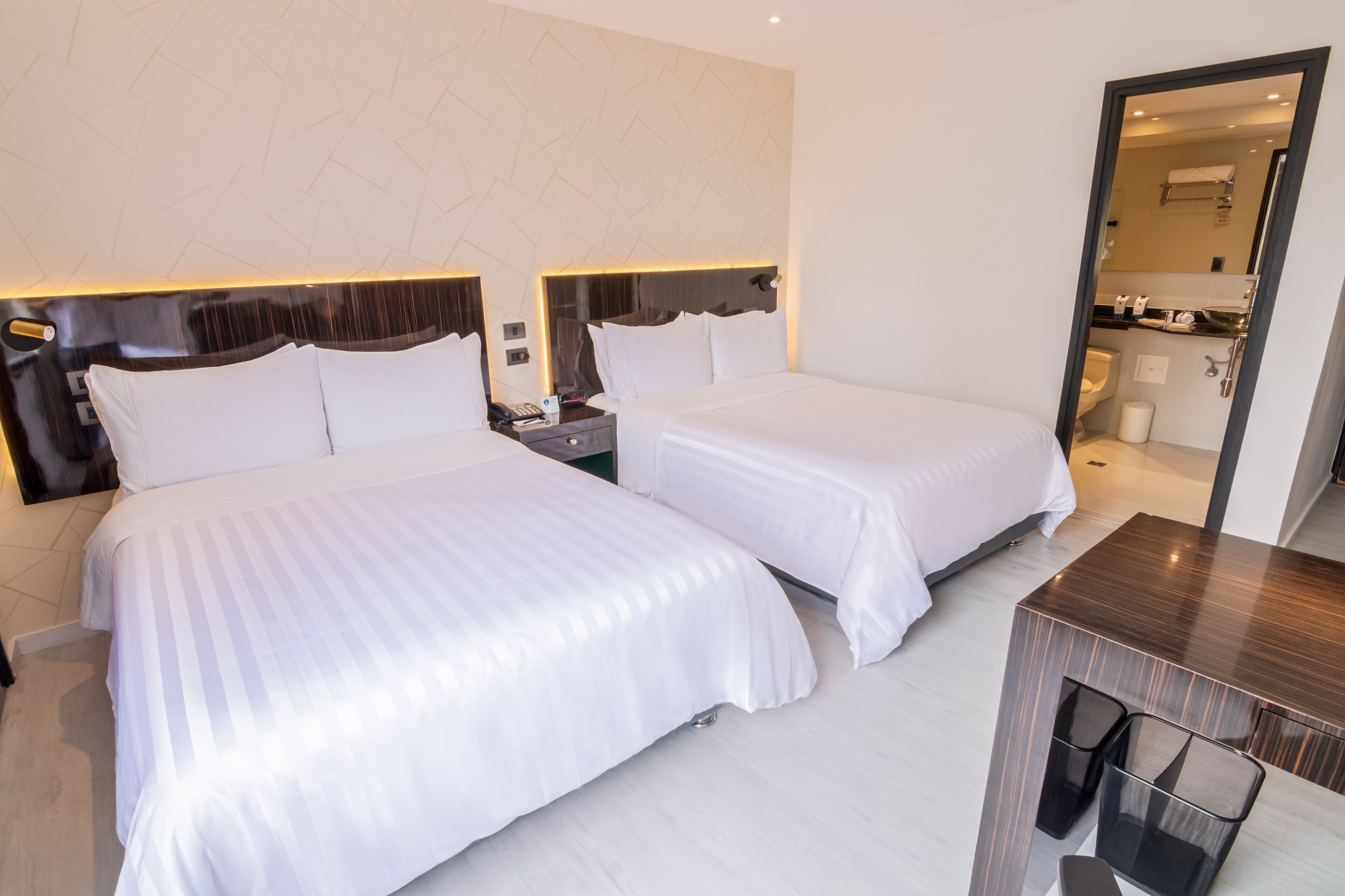 A hotel room with two beds, a desk, and a mirror.