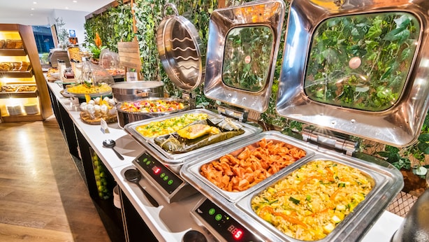 A buffet with various food options, including rice dishes and salads, in a well-lit room with a wooden floor.
