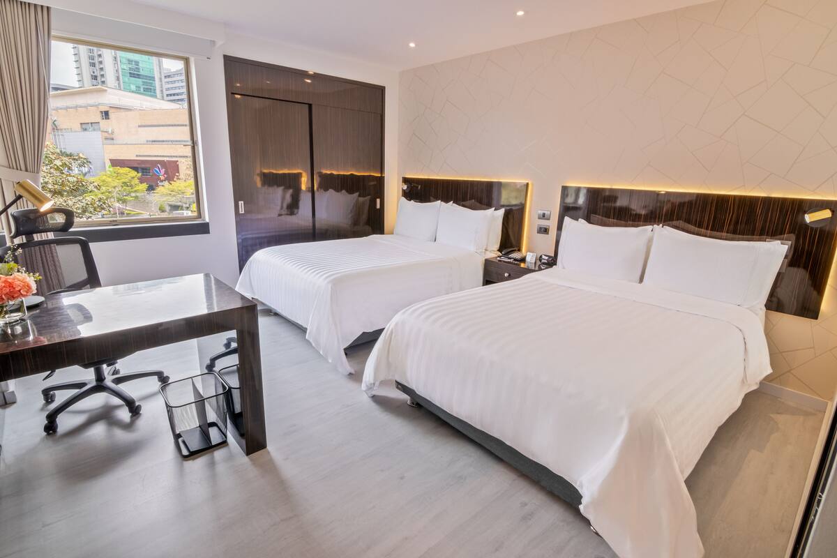A hotel room with two beds, a desk, and a chair.