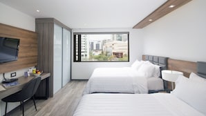 A modern hotel room with two beds, a desk, a TV, and a large window offering a city view.