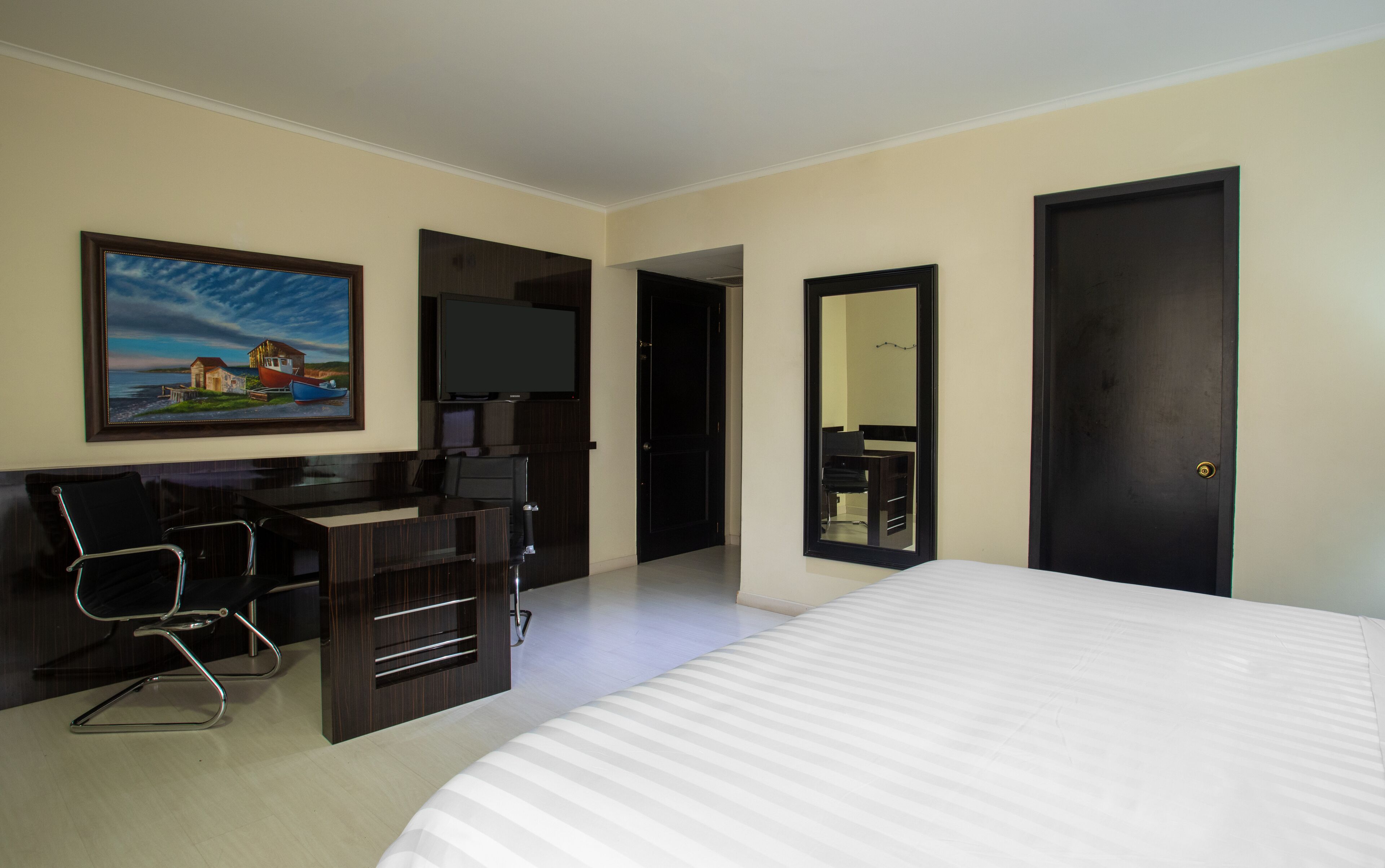 A hotel room with a bed, a desk with a chair, a television, and a painting on the wall.