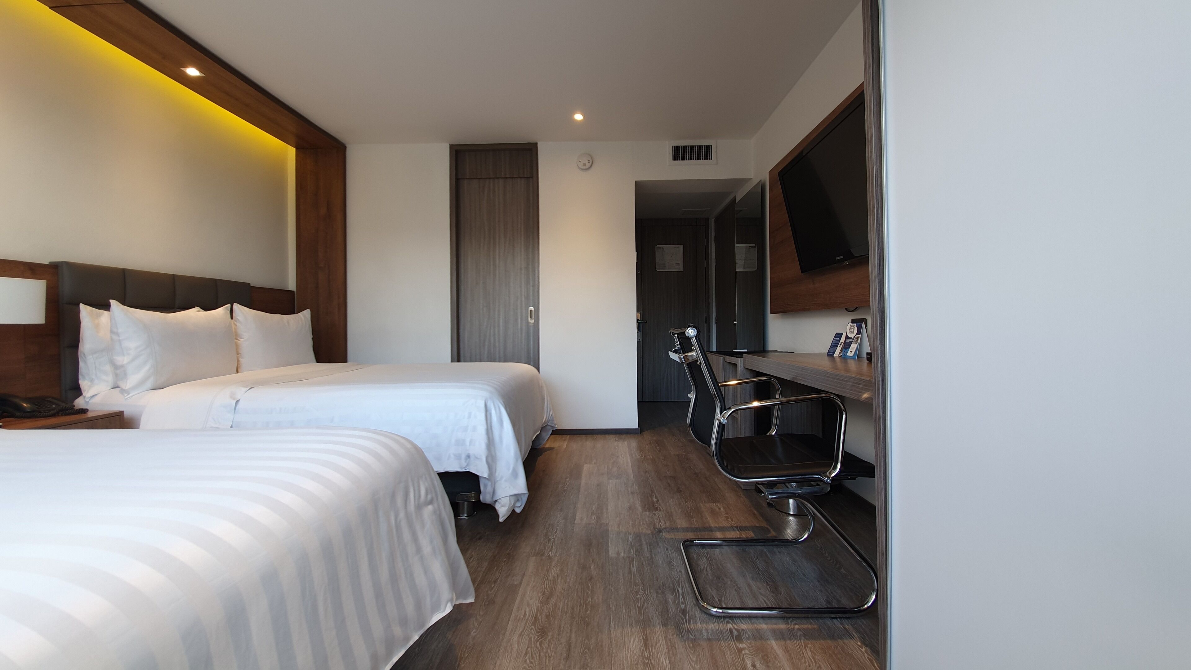 Habitación de hotel con dos camas, un escritorio, una silla, un televisor de pantalla plana y un espejo.