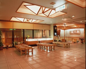 Un intérieur de style japonais traditionnel, avec un sol recouvert de tatamis, des meubles en bois et un espace d’accueil agrémenté d’une horloge et de panneaux d’information.
