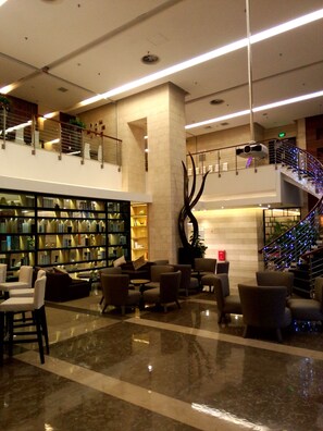 A spacious lobby with a high ceiling, a large bookshelf, comfortable seating areas, and a staircase with decorative lighting. - Somerset Jiefangbei (Chongqing)