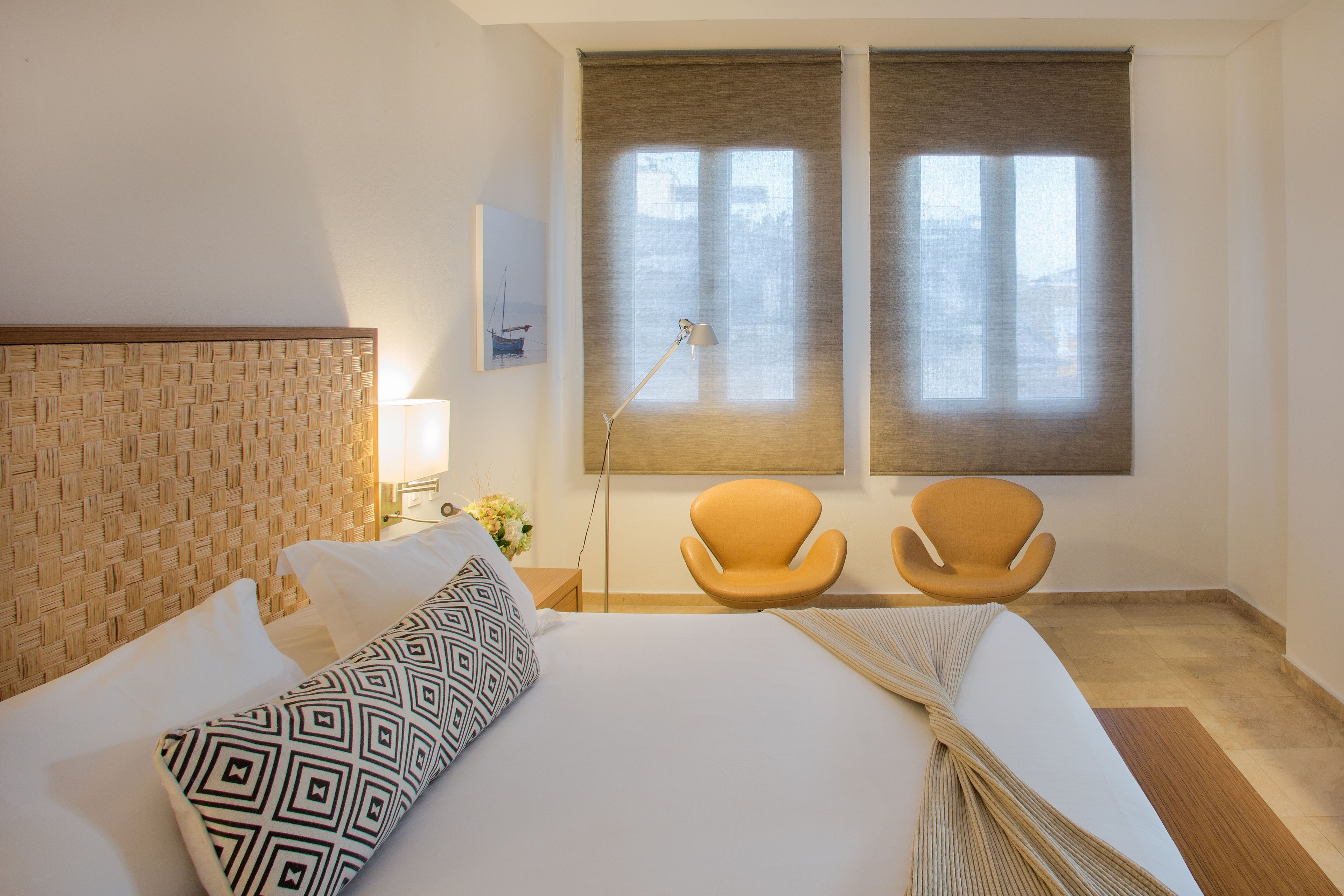 Et hotelværelse med en stor seng, to lænestole, en lampe og et vindue med skodder.