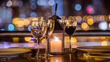 Une table dressée pour le dîner, avec des verres, des assiettes et une bougie, dans une pièce faiblement éclairée, le tout sur fond flou.