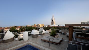 A rooftop terrace with a pool, outdoor seating, and a view of a historic building.