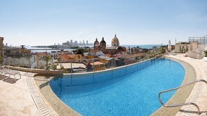 Ein Pool auf dem Dach mit Blick auf eine Stadtlandschaft und ein Gewässer in der Ferne.