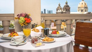 A breakfast table set with croissants, fruit, and coffee on a balcony overlooking historic buildings. - Movich Hotel Cartagena de Indias (Cartagena)