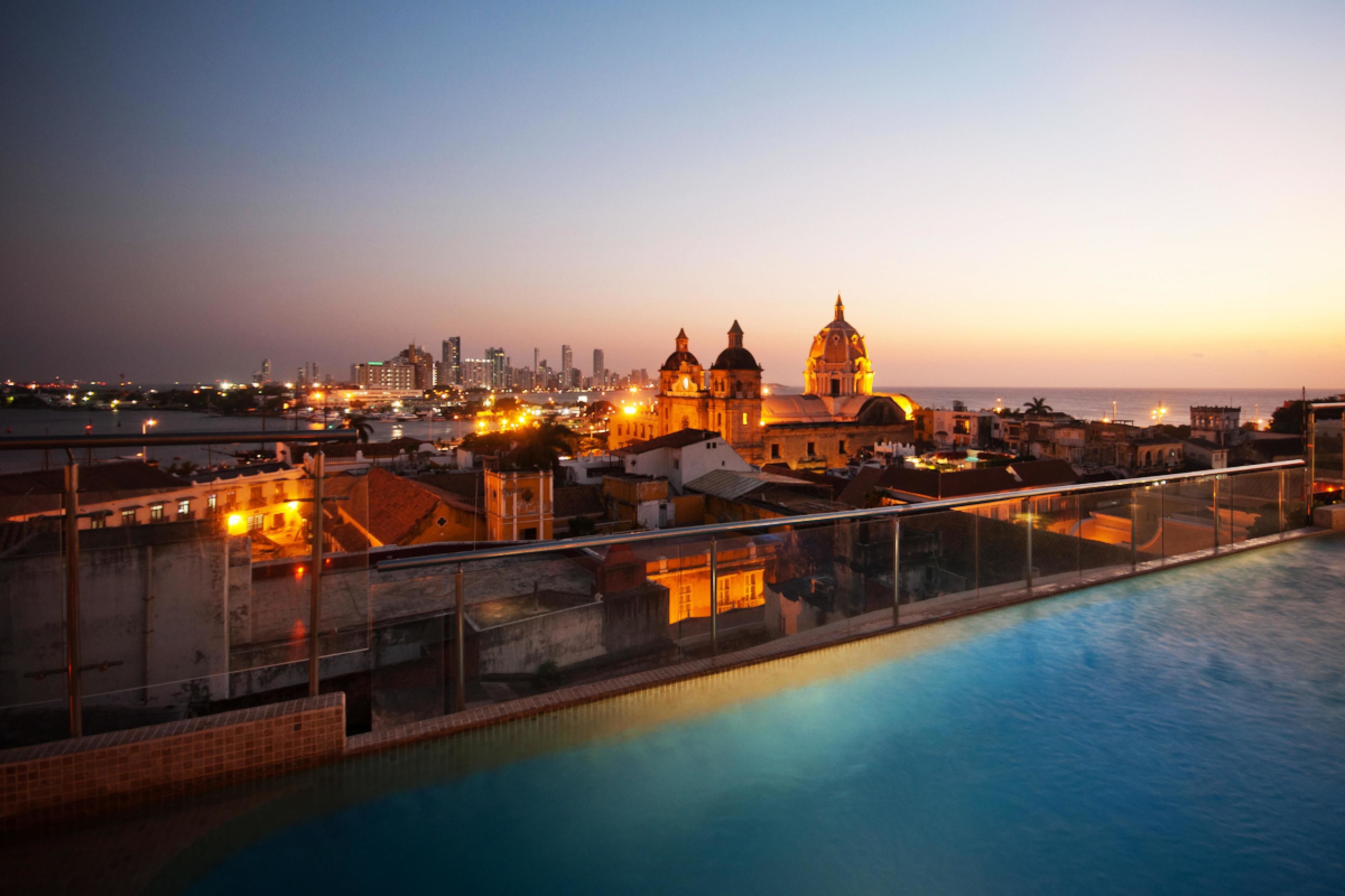 A poolside view of a hotel with a cityscape in the background, including a prominent building with domes.