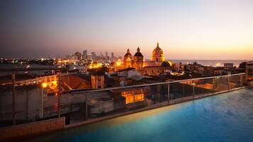 A poolside view of a hotel with a cityscape in the background, including a prominent building with domes.