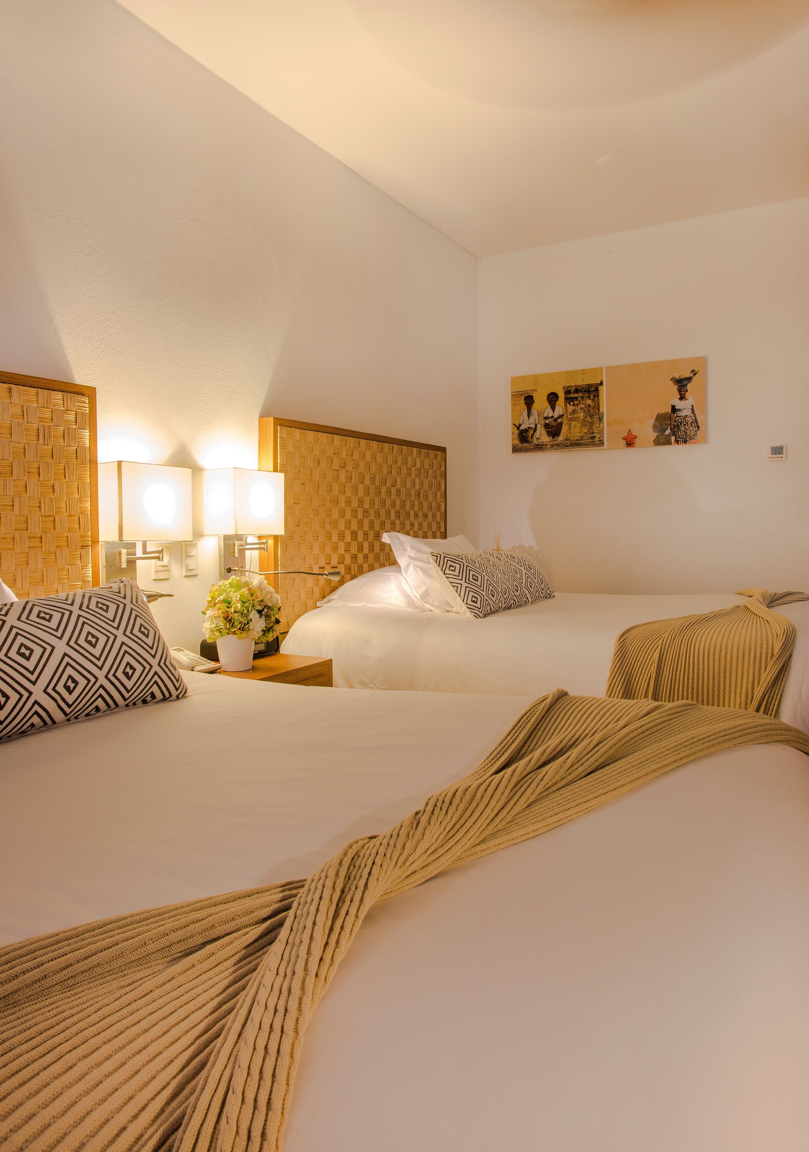 A hotel room with two beds, a wooden headboard, a nightstand with a lamp, and a wall-mounted artwork.