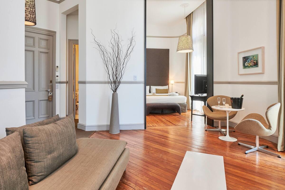 A modern hotel room with a wooden floor, a sofa, a bed, a desk, and a chair.