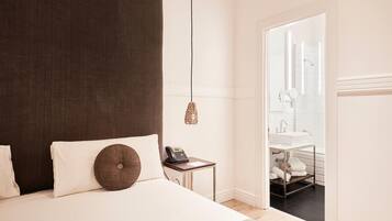 A hotel room with a bed, bedside table with a phone, a hanging lamp, and a view of the bathroom.