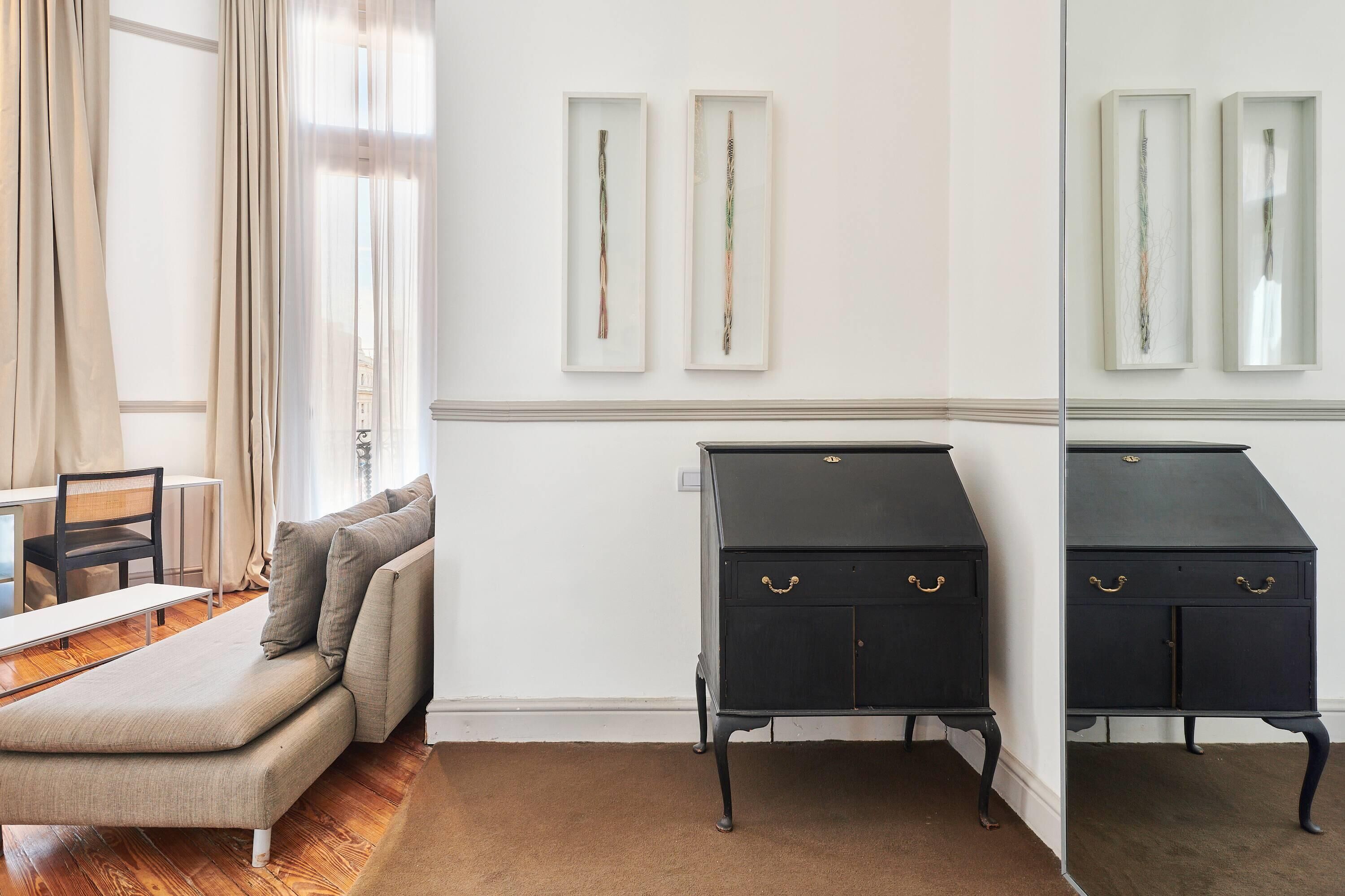 A room with a sofa, a small table, and a black cabinet with gold handles. There are two framed artworks on the wall.
