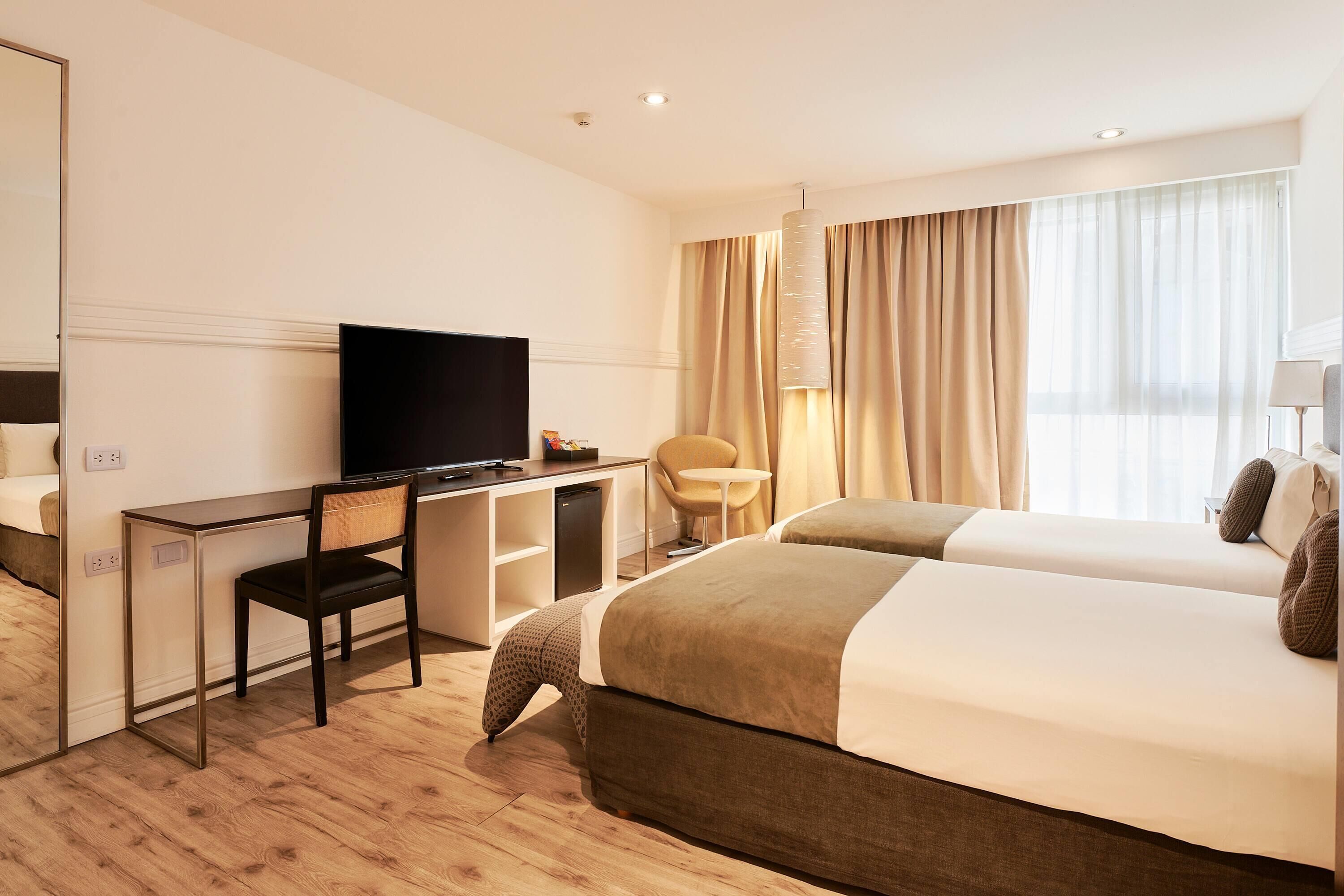 A hotel room with a bed, a desk with a television, a chair, and a small table.