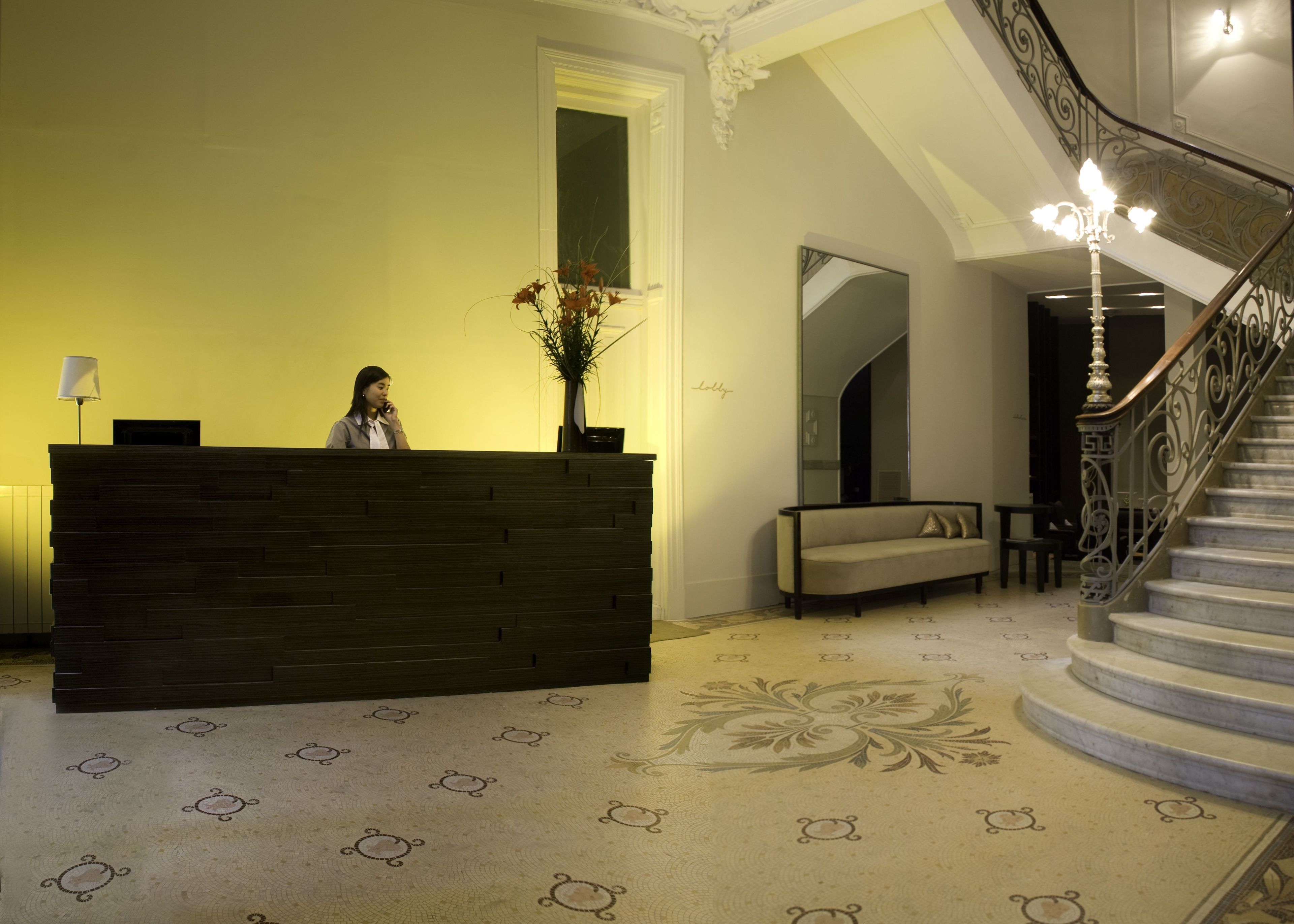 Una recepción con una recepcionista, un espejo, un sofá y una escalera.