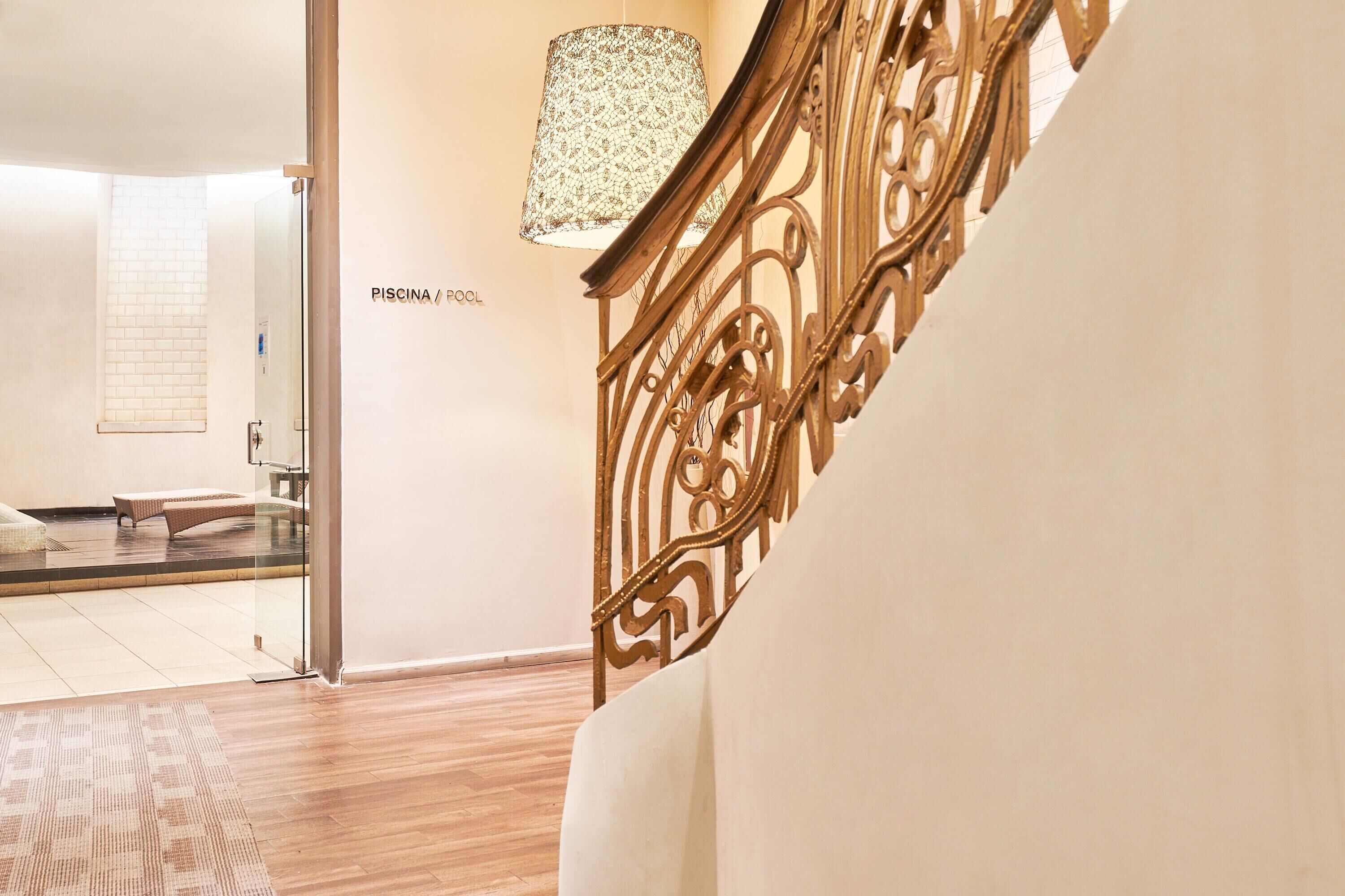 Un interior moderno con una escalera de madera, un vidrio que da a una zona de piscina y una alfombra estampada en el suelo.