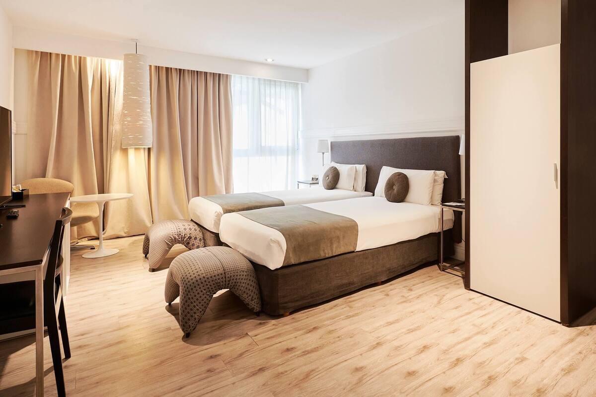 A modern hotel room with a large bed, a desk, a chair, and a wardrobe.