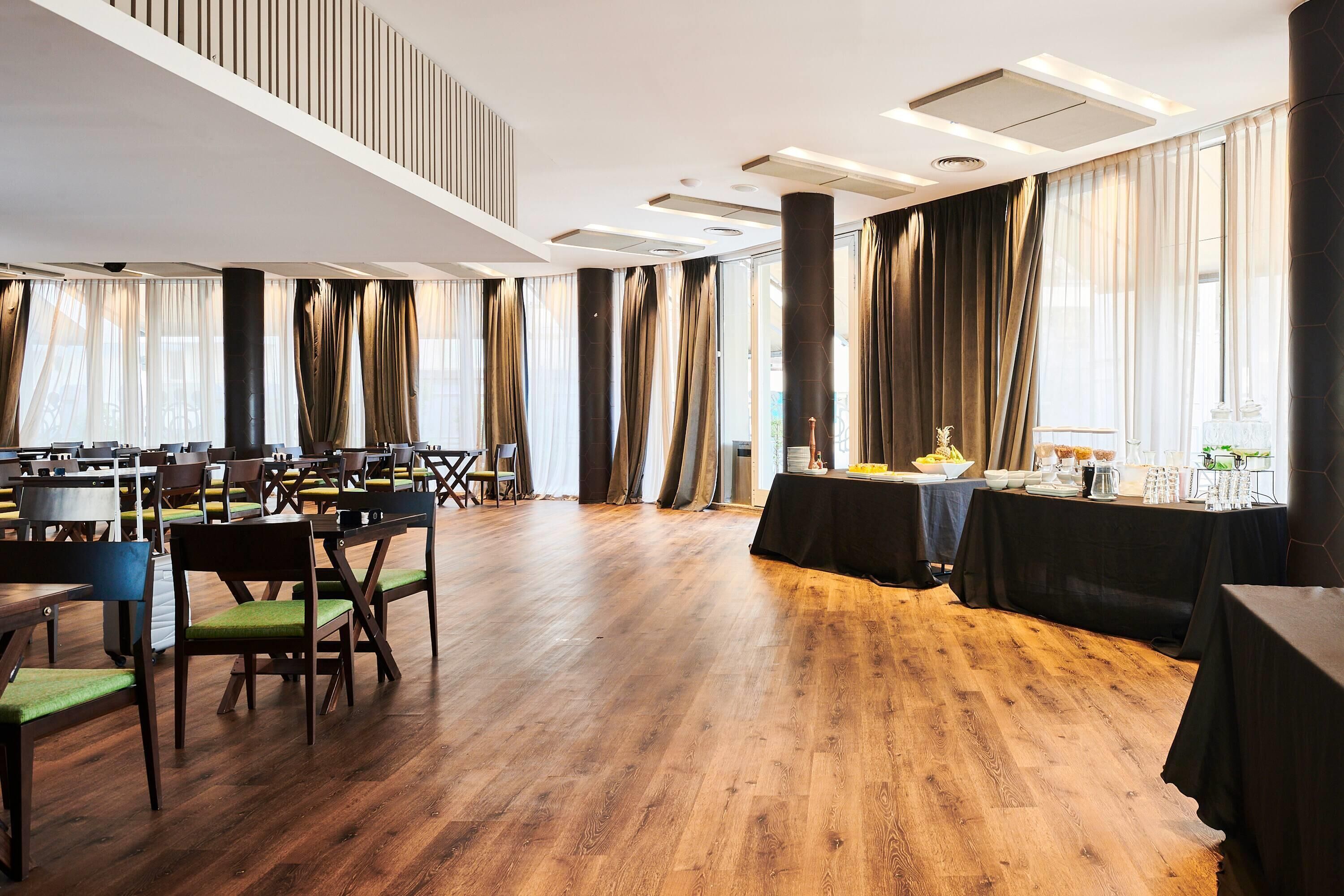 A spacious room with wooden flooring, multiple tables, and chairs arranged for dining.